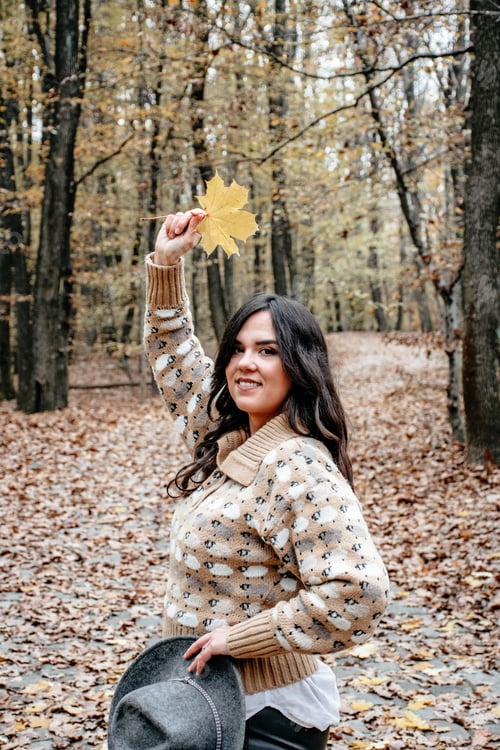 Preview: Shot of a beautiful woman in an autumn forest with a maple leaf on the hand