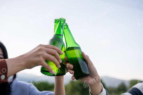 Preview: Close up man and woman friends clinking drink bottle while go on picnic with mountain and sky view.