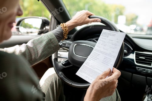 Preview: Hands of contemporary mature businesswoman looking through paper while driving
