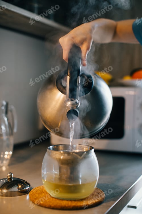 Preview: Person pouring hot water into teapot in kitchen