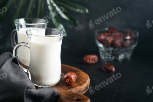 Preview: Ramadan Kareem food and drinks. Plate of dates, glass of milk and date palm branch on black backgrou