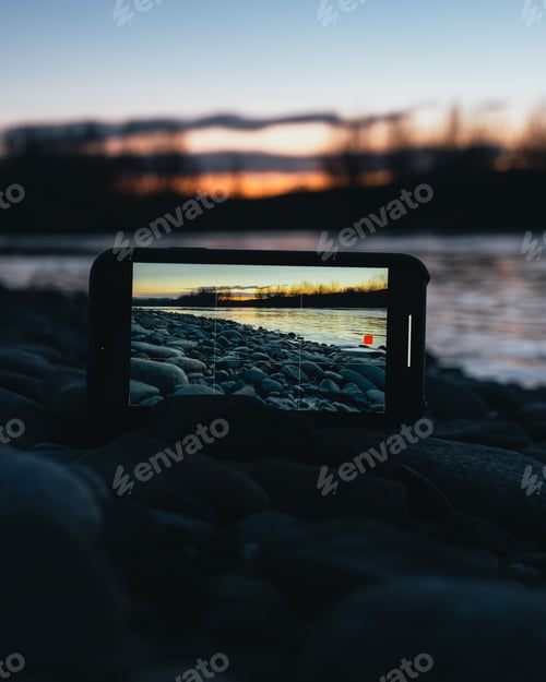 Preview: Smartphone on the coast recording the sunset over the river with tree silhouettes
