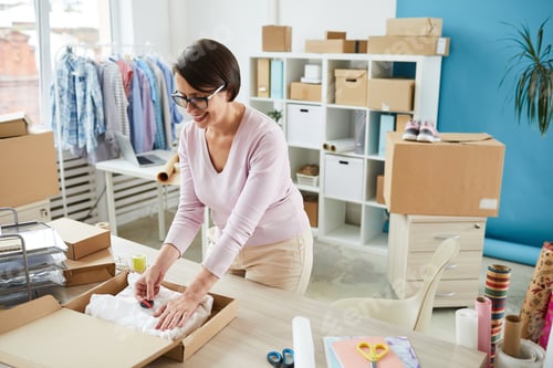 Preview: Worker of online shop office putting sticker on wrapped piece of clothing