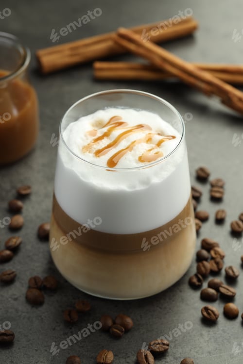 Preview: Tasty latte macchiato in glass, coffee beans and cinnamon on grey table, closeup