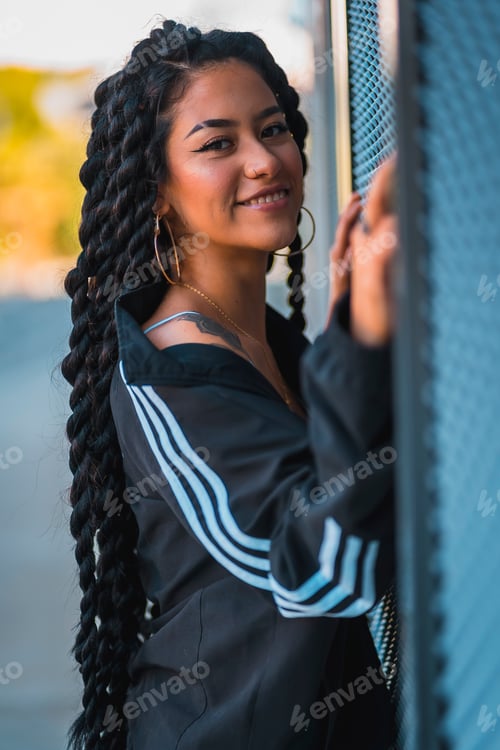 Preview: Urban session. Young black ethnic woman with long braids and with tattoos, looking glass, smiling