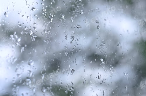 Preview: A photo of rain drops on the window glass with a blurred view of the blossoming green trees