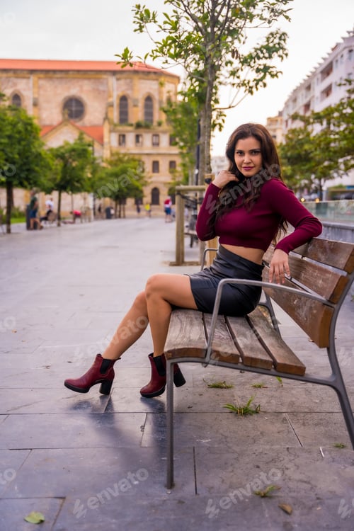 Preview: A brunette woman in a leather skirt sitting in the city, lifestyle, fashion pose, vertical photo