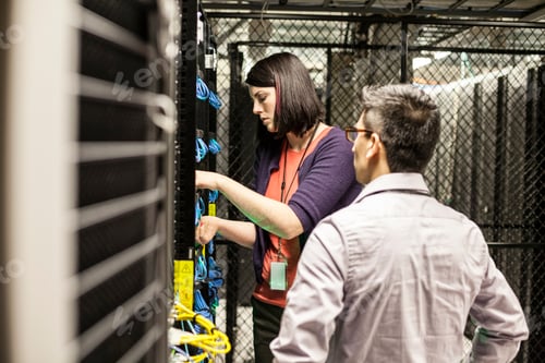Preview: Caucasian woman and man technicians working on CAT 5 cables in a large computer server farm.