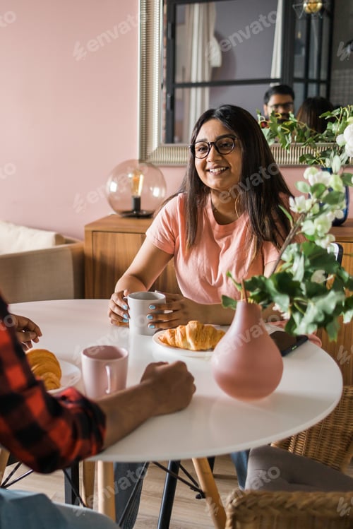 Preview: Happy couple eating breakfast and talking at dining table in morning. Indian girl and latino guy
