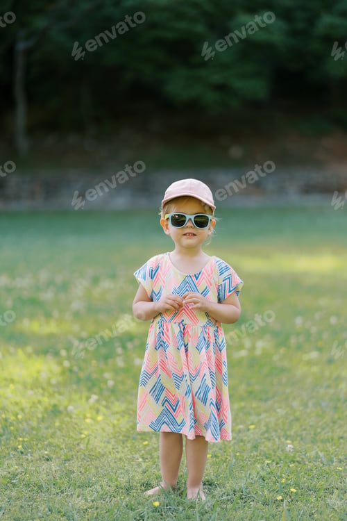 Preview: Little girl in sunglasses stands on a green lawn