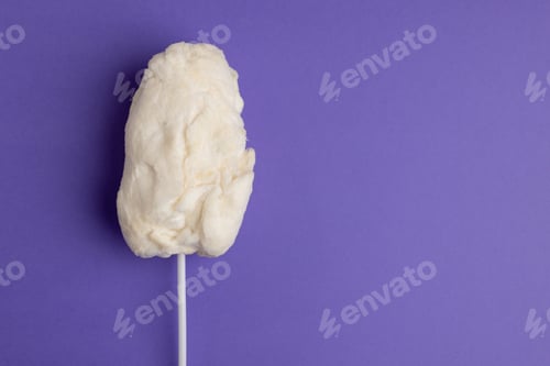 Preview: Horizontal image of homemade white candy floss on stick, on purple background with copy space