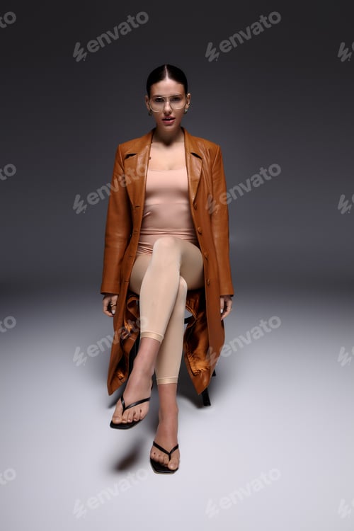 Preview: Stylish young woman in a chic leather coat poses confidently in a modern studio setting