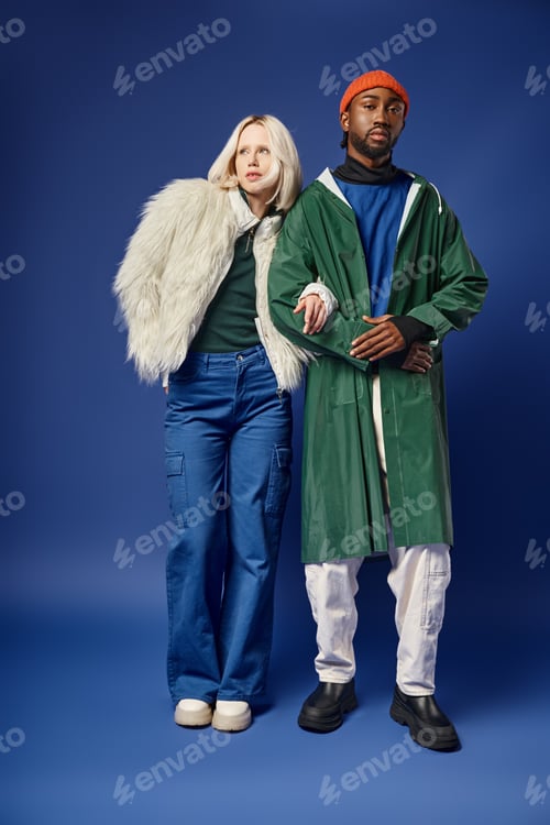Preview: multiethnic couple posing on blue, beautiful woman in white faux fur jacket and african american man