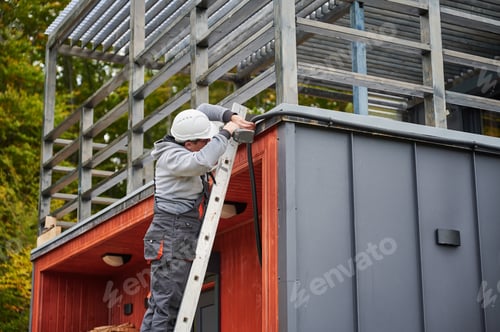 Preview: Man worker prepearing for mounting photovoltaic solar modules on roof of house.