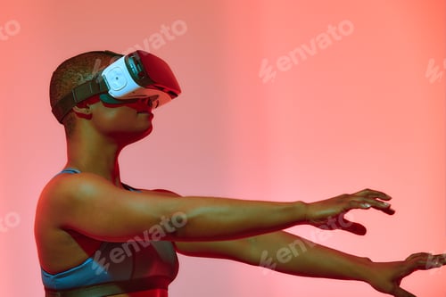Preview: African american woman streamer playing video game using virtual reality glasses at gaming room