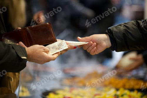Preview: Two unrecognizable people exchange paper currency money at a local outdoor winter food festival