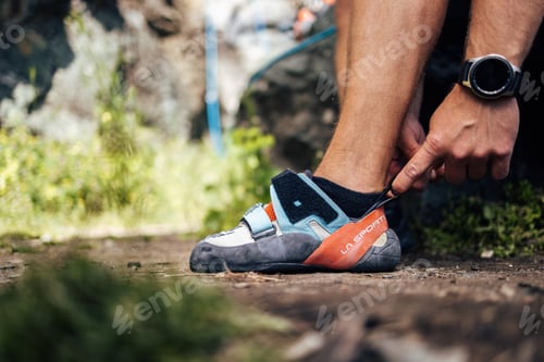 Preview: Close-Up of Hands Adjusting Climbing Shoes on Outdoor Trail
