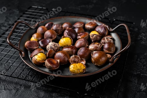 Preview: Cracked roast chestnuts served in a tray. Black background. Top view