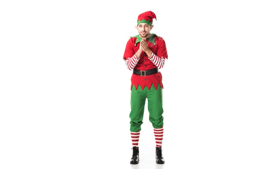 Preview: excited man in christmas elf costume looking at camera and rubbing hands in anticipation isolated on