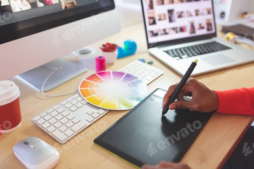 Preview: Close-up of young mixed-race female graphic designer using graphic tablet at desk in a modern office