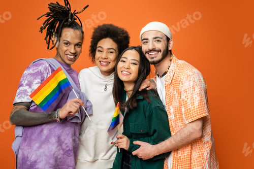 Preview: trendy man with dreadlocks holding lgbt flag near happy multiethnic friends isolated on orange