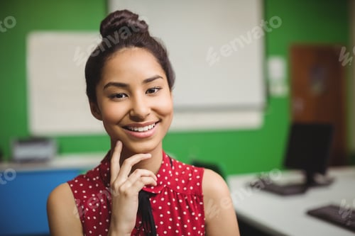 Preview: Portrait of smiling schoolgirl standing with hand on chin in classroom