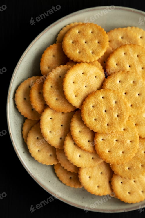 Preview: Salty Round Crackers on a Plate on a black surface, top view. Flat lay, overhead, from above.