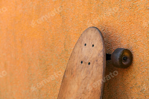 Preview: Worn skate longboard leaning against the dirty orange wall