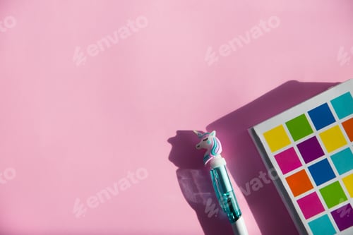 Preview: Colored notebook for notes, funny unicorn pen on pink background. Flat lay. Top view. Copy space