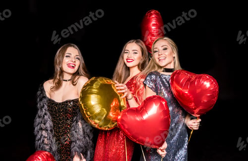 Vista previa: Gorgeous young women in glittering dresses posing with shiny balloons isolated on black