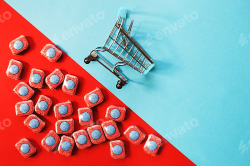 Preview: capsules for kitchen dishwashers and shopping cart on a blue and red background. flat lay