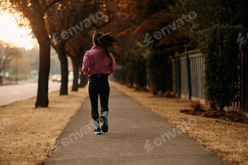 Preview: Back view of female athlete running on the street.