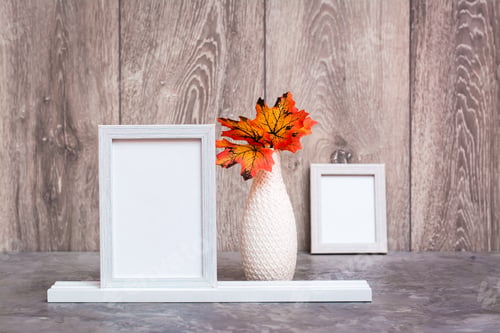 Preview: Two empty photo frames on a stand and a vase with orange maple leaves stand on the table