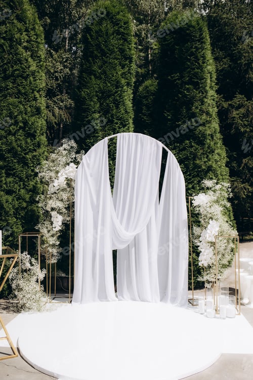 Preview: Elegant Outdoor Wedding Arch Decorated With White Drapes and Flowers