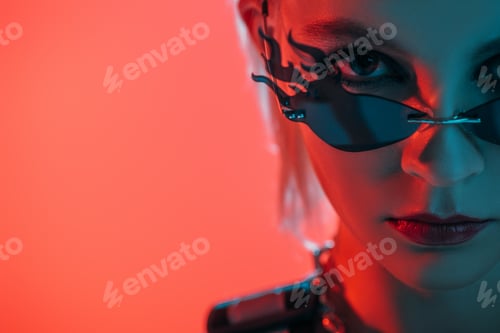 Preview: stylish futuristic girl posing in fire-shaped sunglasses on pink in red light