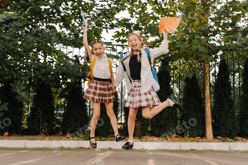 Preview: Two happy schoolgirls jumping with joy on the first day of school