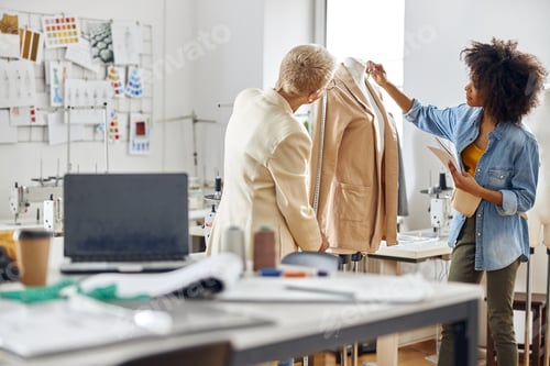 Preview: African-American lady with mature colleague fashion designers at work apon jacket in workshop