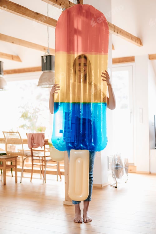 Preview: Young woman standing barefoot in her flat with an ice lolly shaped airbed