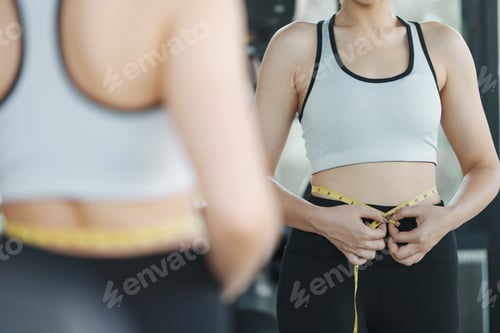 Preview: Young woman measuring her waist by measure tape at the gym.