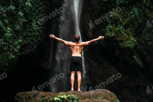 Preview: Back view of a man standing by waterfalls with arms outstretched