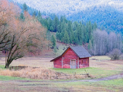Preview: Small red barn in a field by hills.