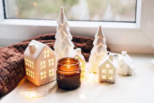 Visualização: Cena de Natal aconchegante com casas de cerâmica e luz de velas perto de uma janela
