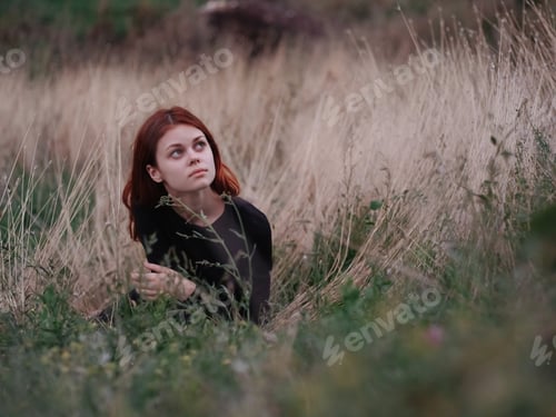 Preview: red-haired woman in a black dress lies in a field on dry grass in nature