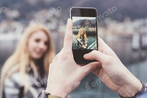 Preview: Man's hands taking smartphone photograph of girlfriend on waterfront, Lake Como, Italy