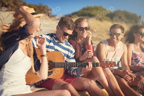 Preview: Cropped shot of a handsome young man playing a guitar for his friends on a summers day at the beach