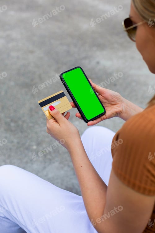 Preview: Closeup of a woman holding a smartphone with a green screen and a card.Online shopping concept
