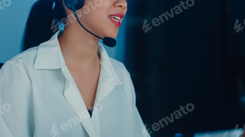 Preview: Millennial Asia young call center agent using computer and microphone headset working.