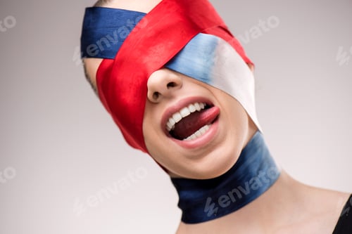 Preview: Woman with wrapped face with ribbons sticking tongue out isolated on grey