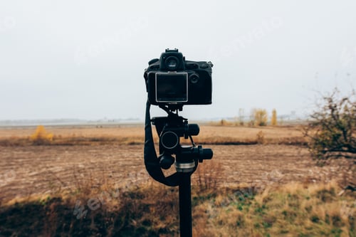 Preview: Selective focus of digital camera on tripod in grassy field