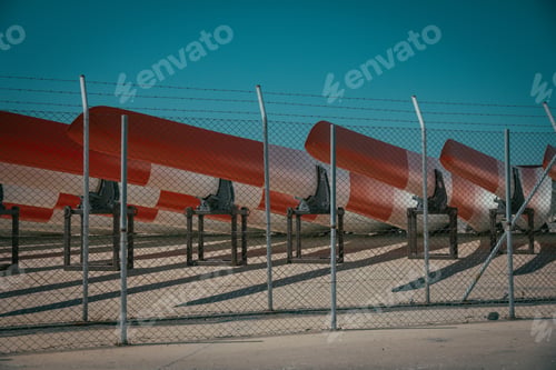 Preview: Metal fence with barb wire and metal canoes behind it with blue sky in the background